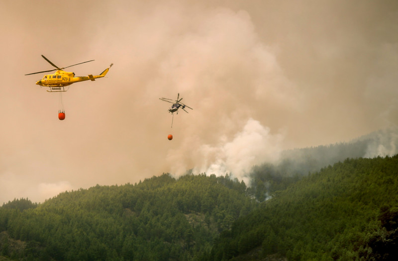  Helicopters fly over the area of Pico Cho Marcial in Arafo to drop water over a huge wildfire raging through forested areas that surround the Mount Teide volcano natural park, on the Canary island of Tenerife, on August 20, 2023. - Firefighters made gains in their battle against a vast wildfire on Tenerife today after better-than-expected overnight weather helped them keep the blaze from destroying homes on the Spanish holiday island. The huge fire broke out late on August 15, 2023 in a mountainous northeastern area, quickly morphing into the Canary Islands' biggest-ever. So far the blaze, which has a perimeter of 84 kilometres (52 miles), has burned through 11,600 hectares (28,700 acres), or just over 6% of Tenerife island, forcing more than 12,000 people to flee their homes. (Photo by DESIREE MARTIN / AFP)