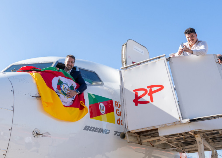 Governador Eduardo Leite exibe a bandeira do RS no primeiro avião que pousou no Salgado Filho em Porto Alegre